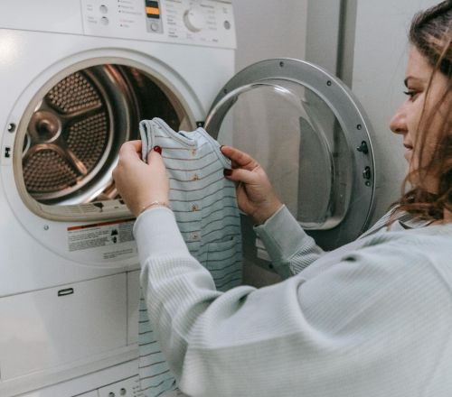 Side view of crop female in casual outfit looking at baby bodysuit before washing clothes in laundry room