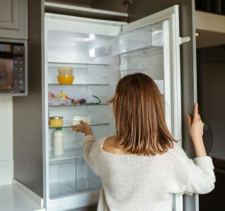 A woman reaches into a refrigerator in a contemporary kitchen, creating a lifestyle moment.