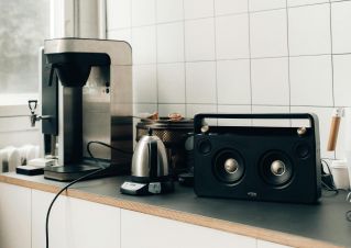Clean minimalist kitchen setup with coffee maker and audio speaker on countertop.
